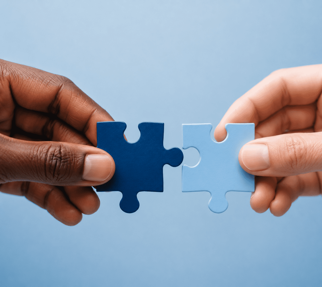 Hands of two different people fitting puzzle pieces together.